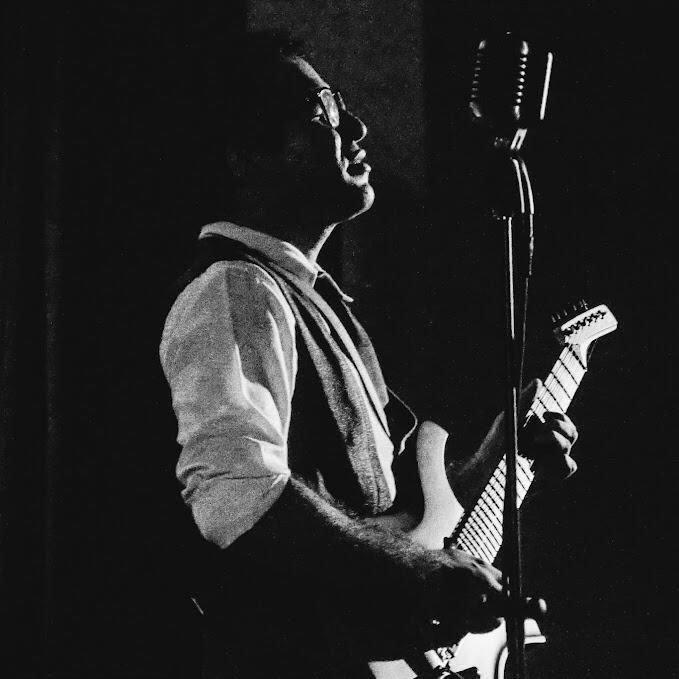 Side view of Everton Vidal Azevedo singing and playing guitar during a Camerata del Oriente concert - Una Canción Hecha Mujer- black-and-white photography (by Antonio Dávila).