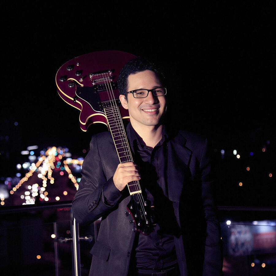 Night session above Scz (by Claudio Arduz) Everton Vidal Azevedo smiling while holding a red semiacoustic guitar on a rooftop (Hotel Cortez) in Santa Cruz de la Sierra, photo by Claudio Arduz.
