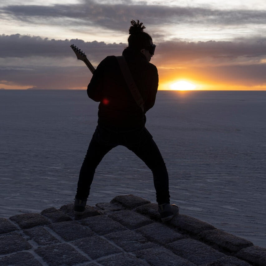 Everton Vidal Azevedo performing with a electric guitar during golden hour on the Salar de Uyuni (Sky Staircase), photo by Marvin Montes.