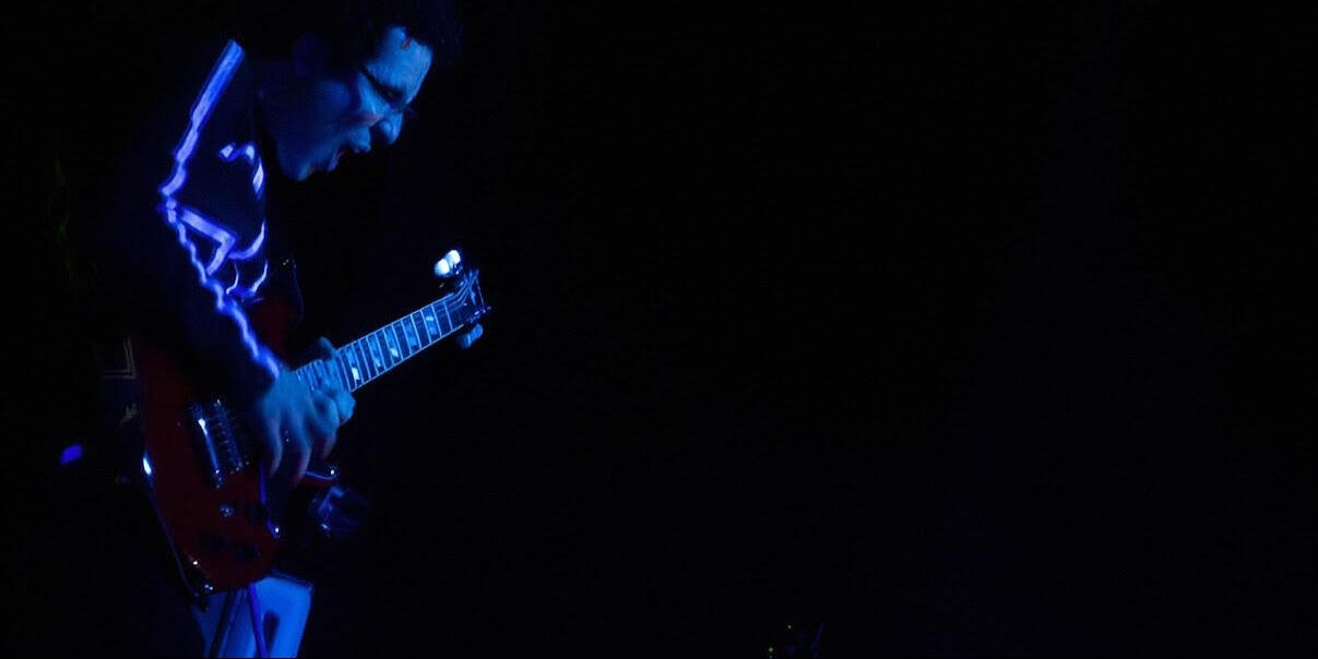 Live performance – blue stage lights Everton Vidal Azevedo performing live on electric guitar, silhouetted in blue stage lighting.