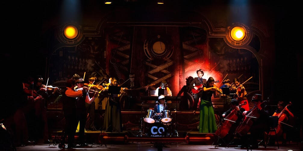 Concert with the Camerata del Oriente (Máquinas). Everton Vidal Azevedo performing with the Camerata del Oriente in a full-orchestra concert with dramatic stage lighting.