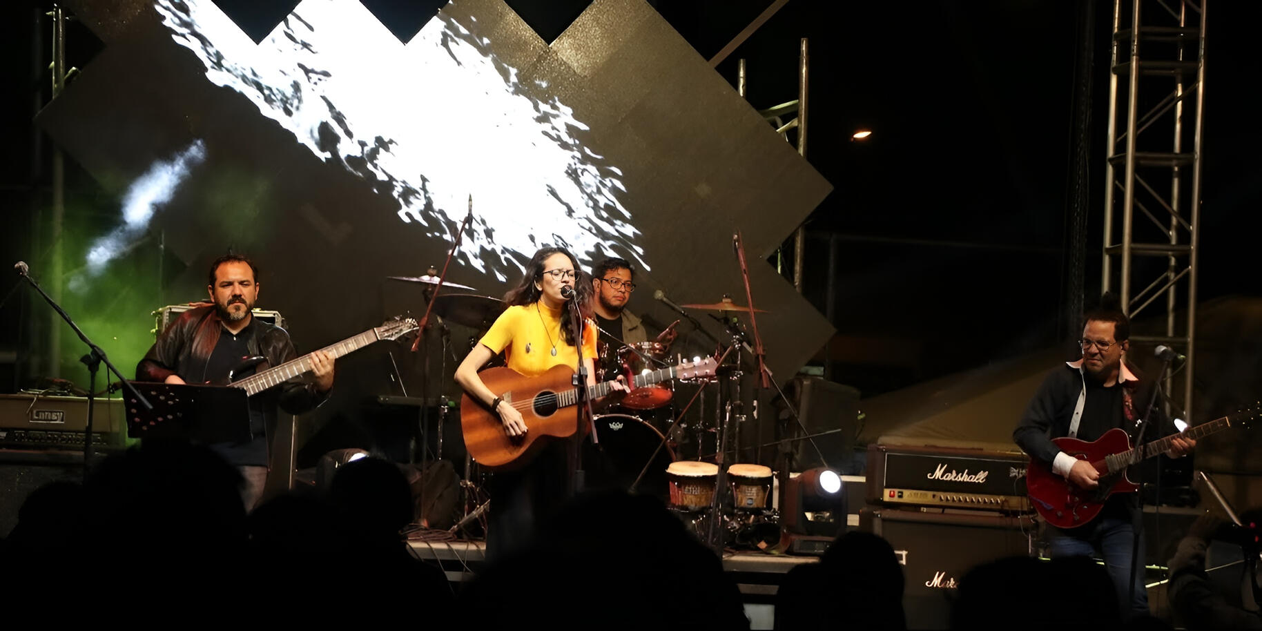 Everton Vidal on stage with Mila Magal at the Alternx Festival, playing guitar under colorful lights, captured by photographer Andru