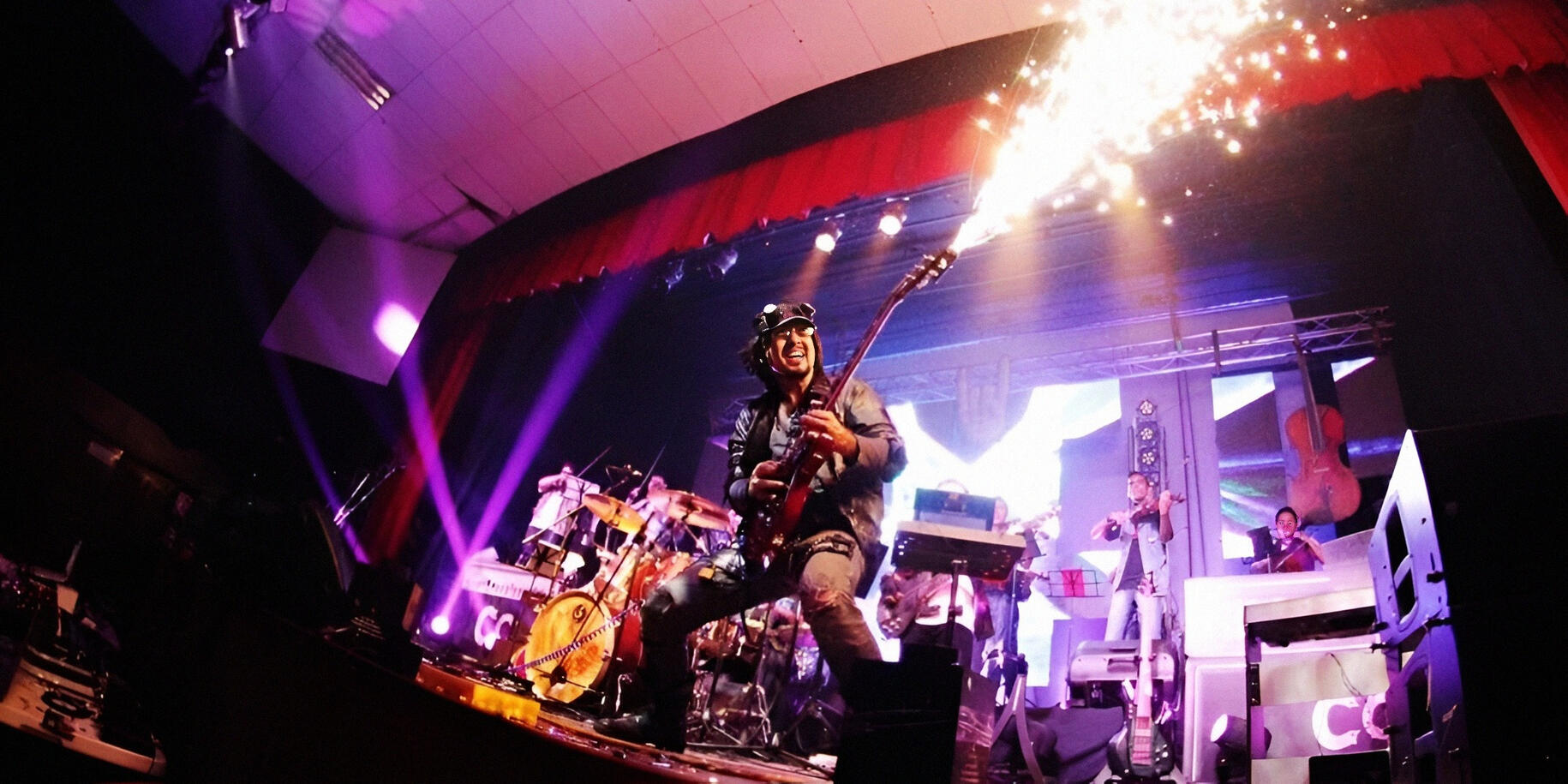 Everton Vidal Azevedo performing live with an electric guitar emitting pyrotechnic sparks during a high-energy concert.